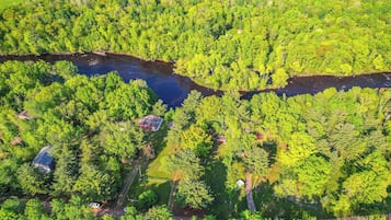 An aerial view of a forested area with a river, several houses, and a clear sky.