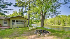 A cabin with a fire pit and two chairs by a lake. - Riverfront Nature Getaway Near Downtown Pine City! (Pine City)