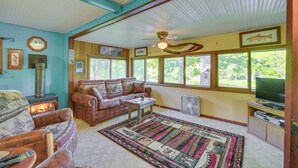 A cozy living room with a fireplace, leather sofa, and a large window with a view of trees. - Riverfront Nature Getaway Near Downtown Pine City! (Pine City)