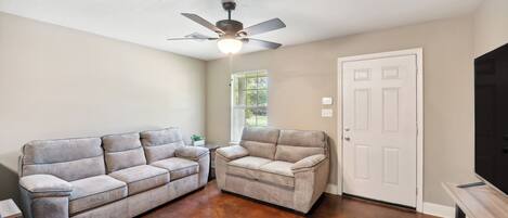 A living room with a ceiling fan, a white door, and a television on a stand.