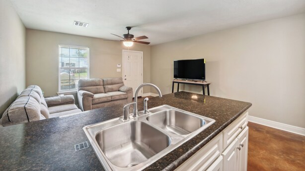 A kitchen with a double sink, a ceiling fan, a television, and a window with blinds. - Lovely Lake Charles Duplex in Central Location! (Lake Charles)