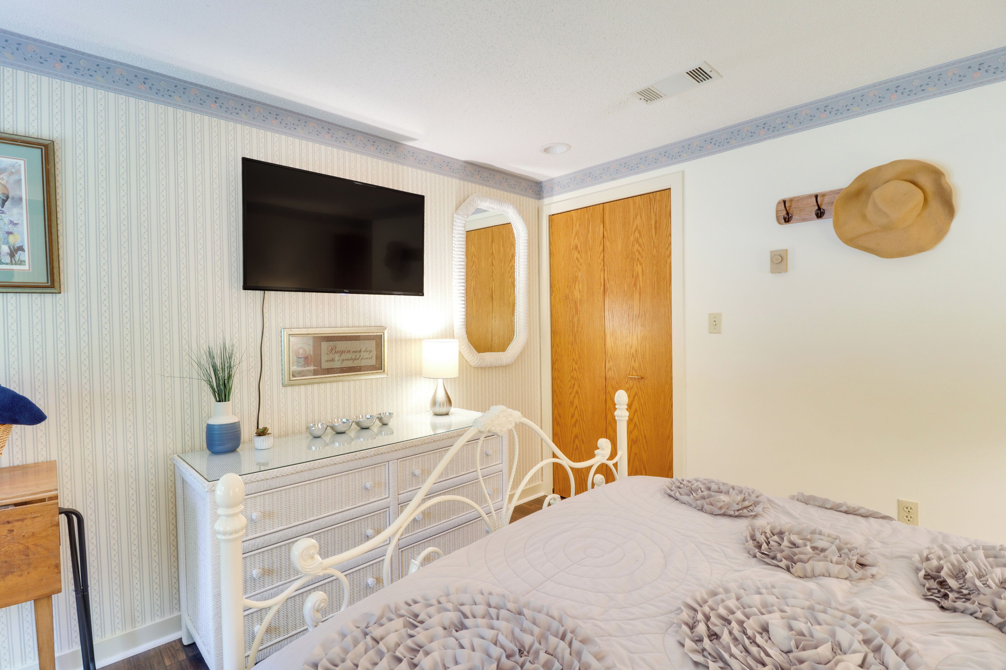 A bedroom with a bed, dresser, mirror, television, and a hat on the wall.