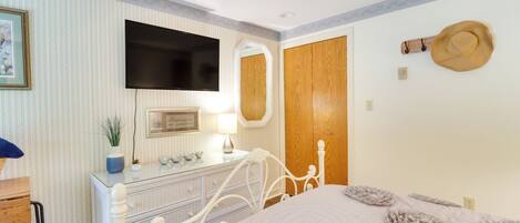 A bedroom with a bed, dresser, mirror, television, and a hat on the wall.