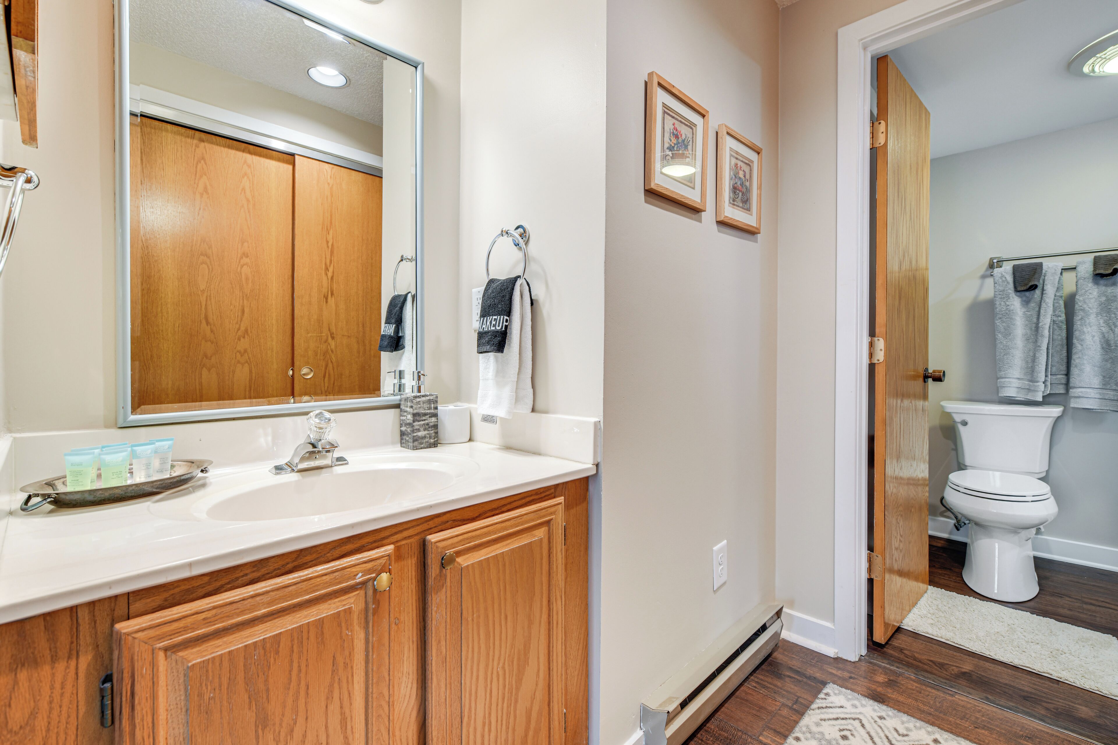 A bathroom with wooden cabinets, a large mirror, a sink, and a toilet.