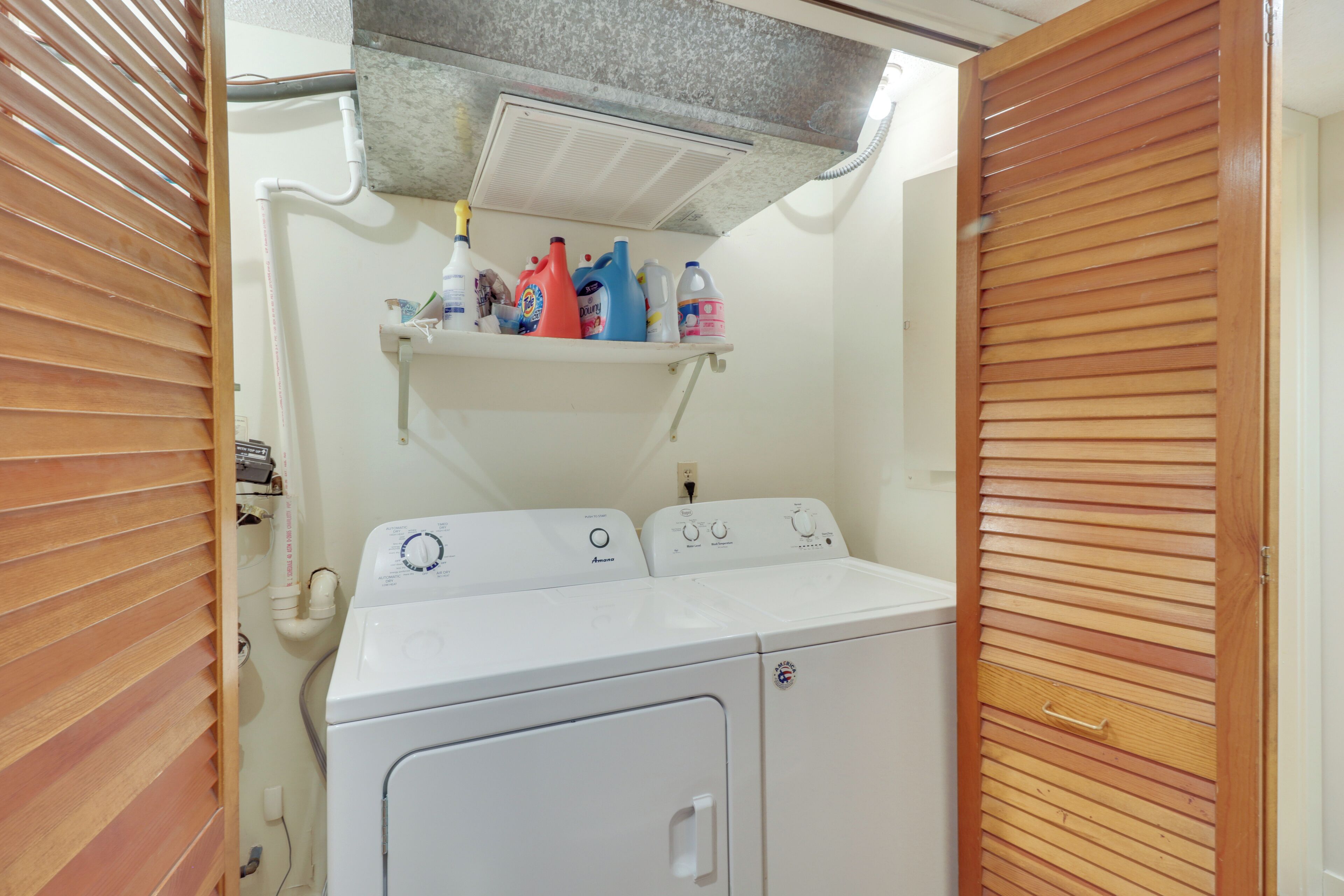 A laundry room with a washing machine, dryer, and a shelf with various cleaning products.