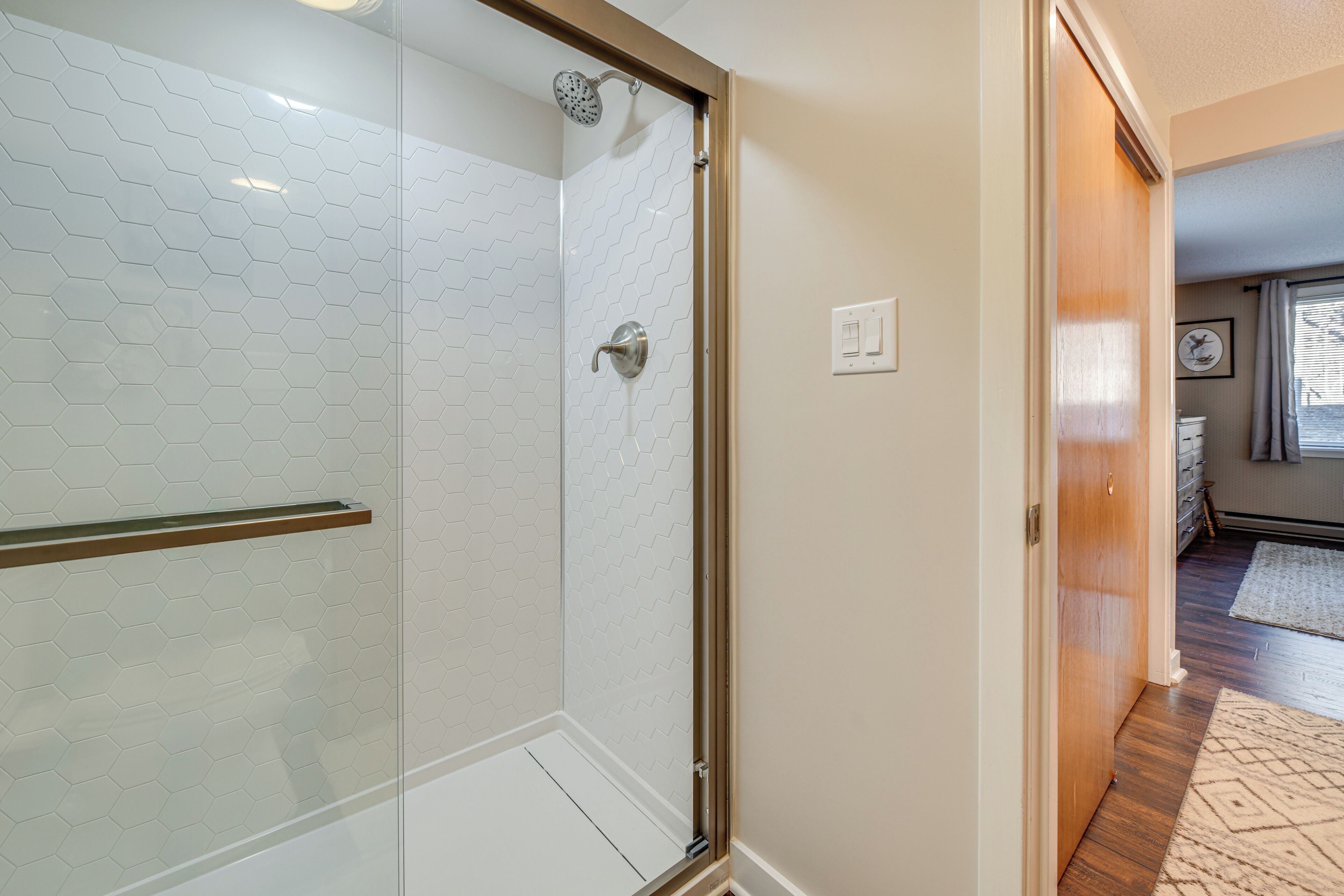 A modern bathroom with a glass shower enclosure, a wooden door, and a visible towel rack.