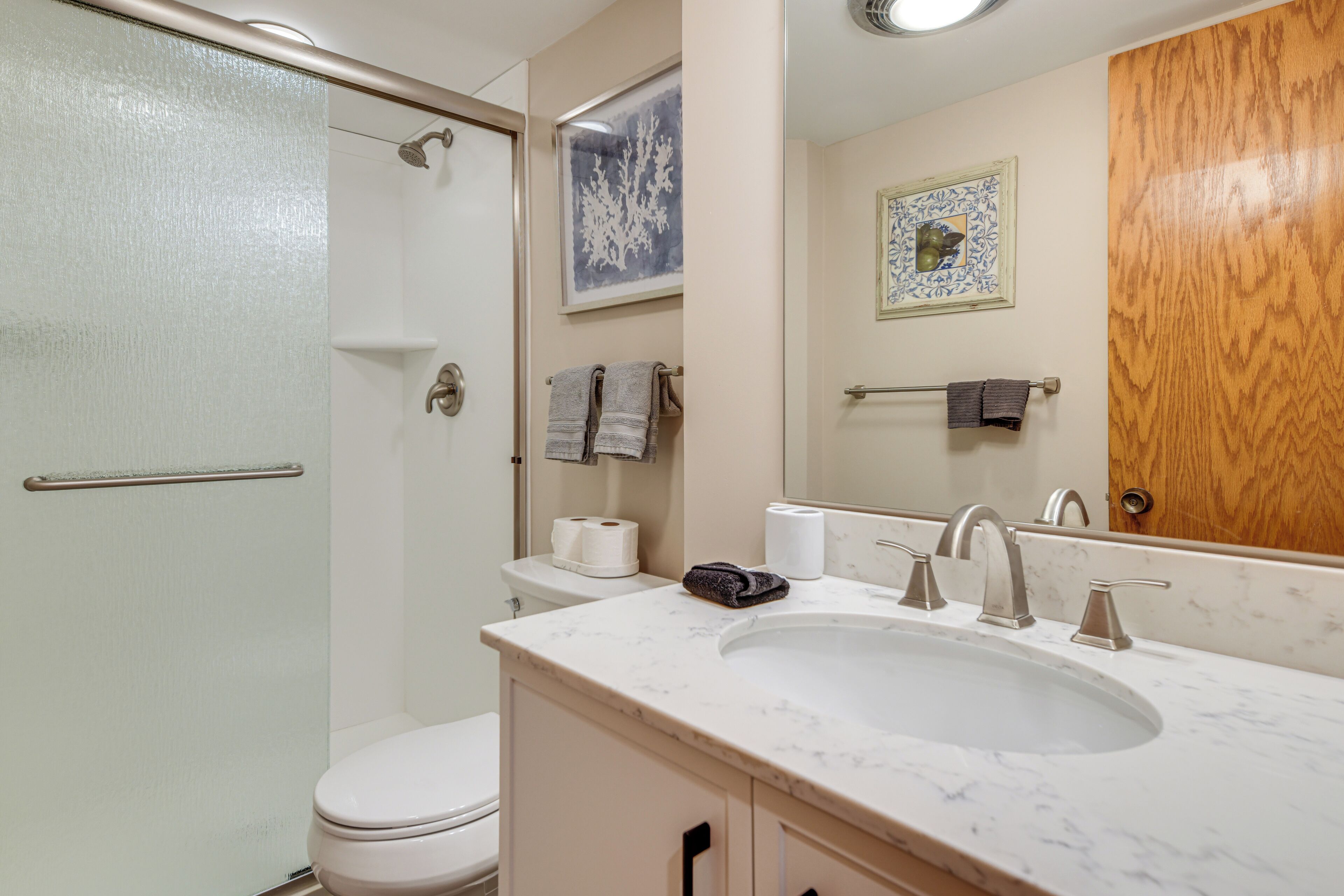A bathroom with a toilet, sink, and shower. There are towels hanging on the wall and a mirror above the sink.