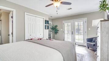 A bedroom with a large bed, a ceiling fan, and a view of the outside through a door.