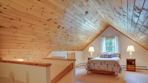 A bedroom with a sloped ceiling, a bed with a floral bedspread, two bedside lamps, and a window with a view of greenery. - Pet-friendly Conway Cabin ~ 5 to Campton Mountain! (Thornton)