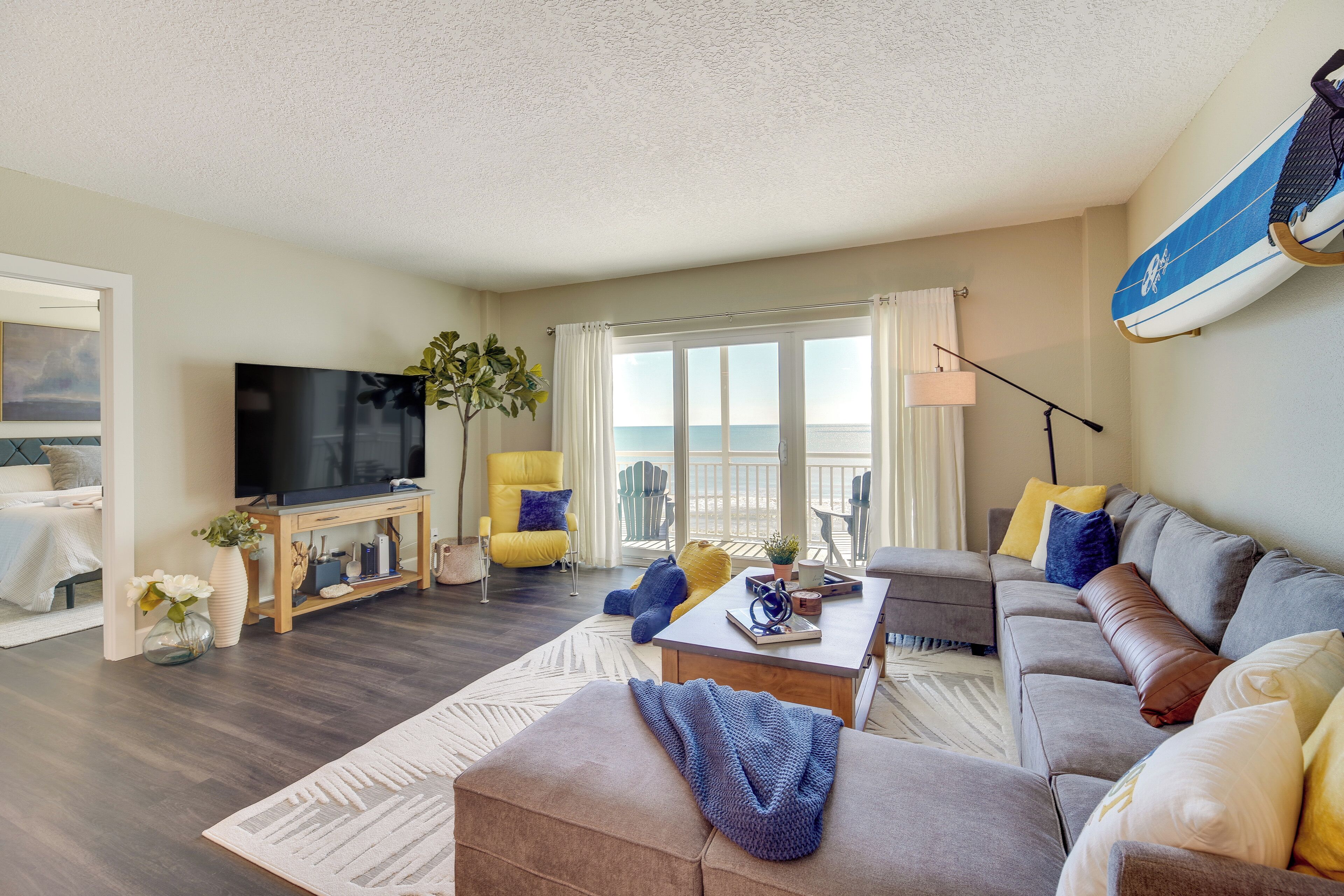 A living room with a sofa, coffee table, TV, and a view of the ocean.