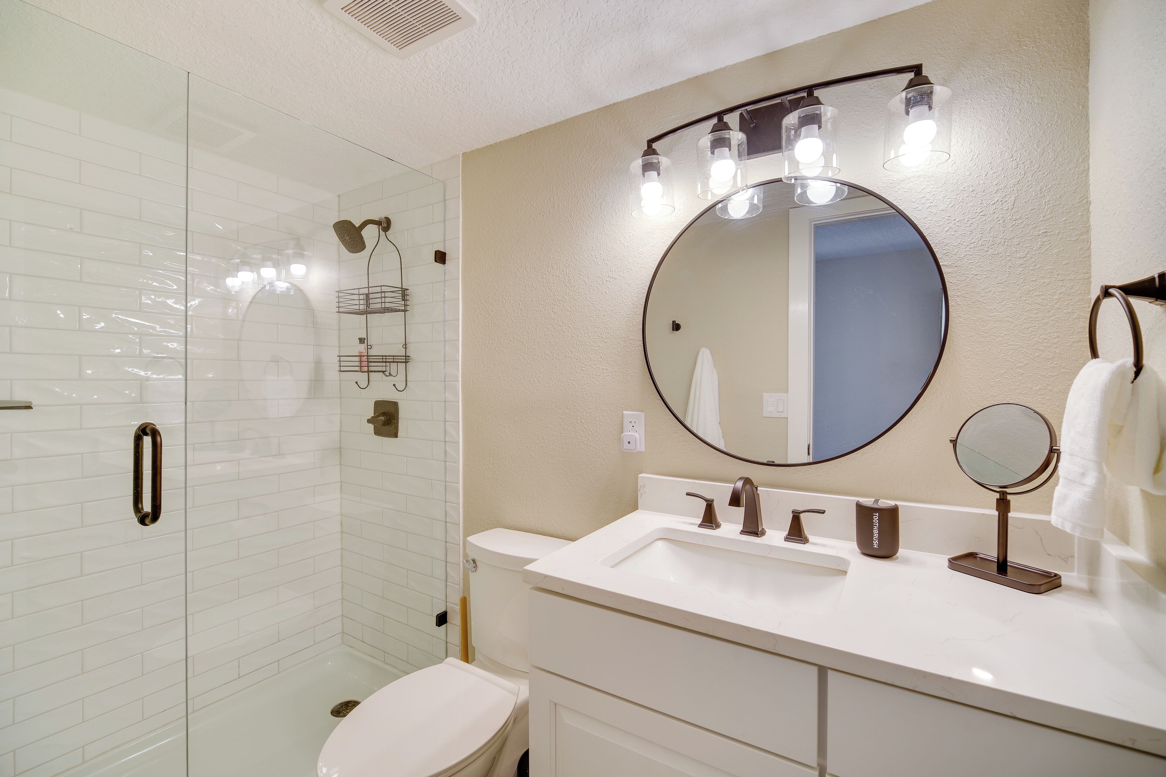 Une salle de bain avec une douche à parois de verre, des toilettes blanches, un lavabo avec un miroir et un porte-serviettes.