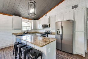 Una cocina moderna con armarios blancos, encimera de granito, electrodomésticos de acero inoxidable y techo de madera.