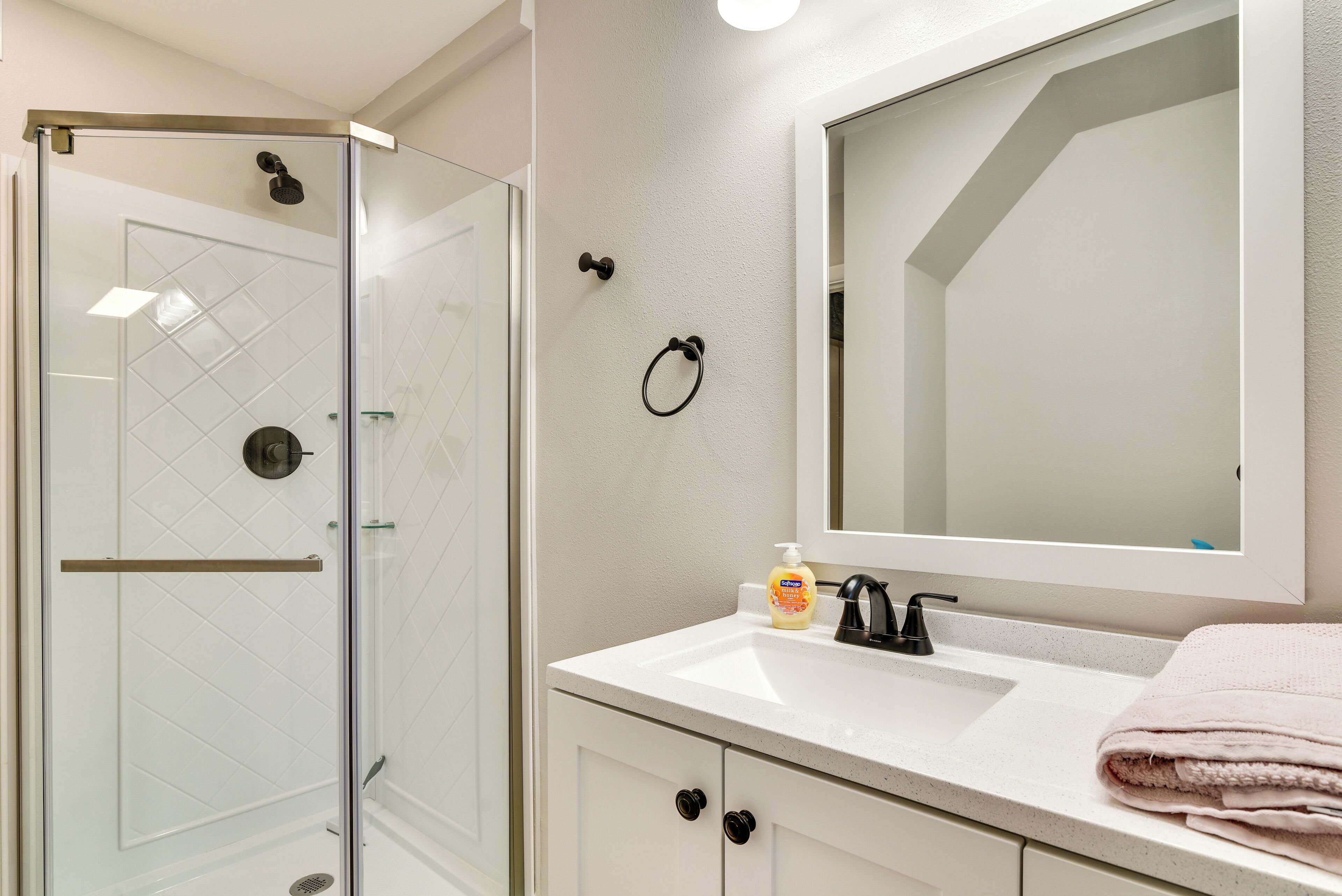 A bathroom with a glass shower enclosure, a white sink with a mirror above it, and a towel on the counter.