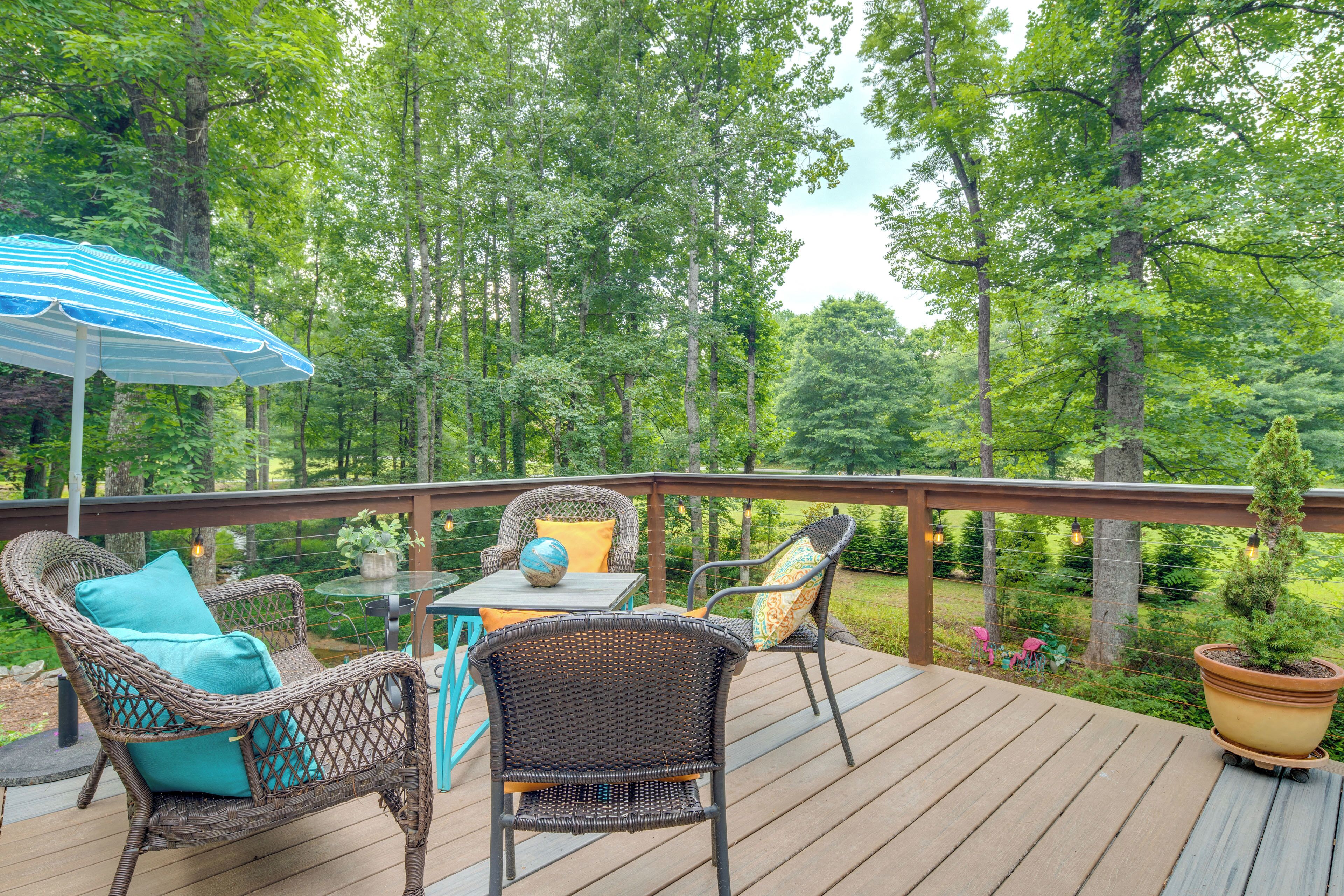 Une terrasse en bois, agrémentée de meubles en osier et d’une table, le tout entouré d’une végétation luxuriante.