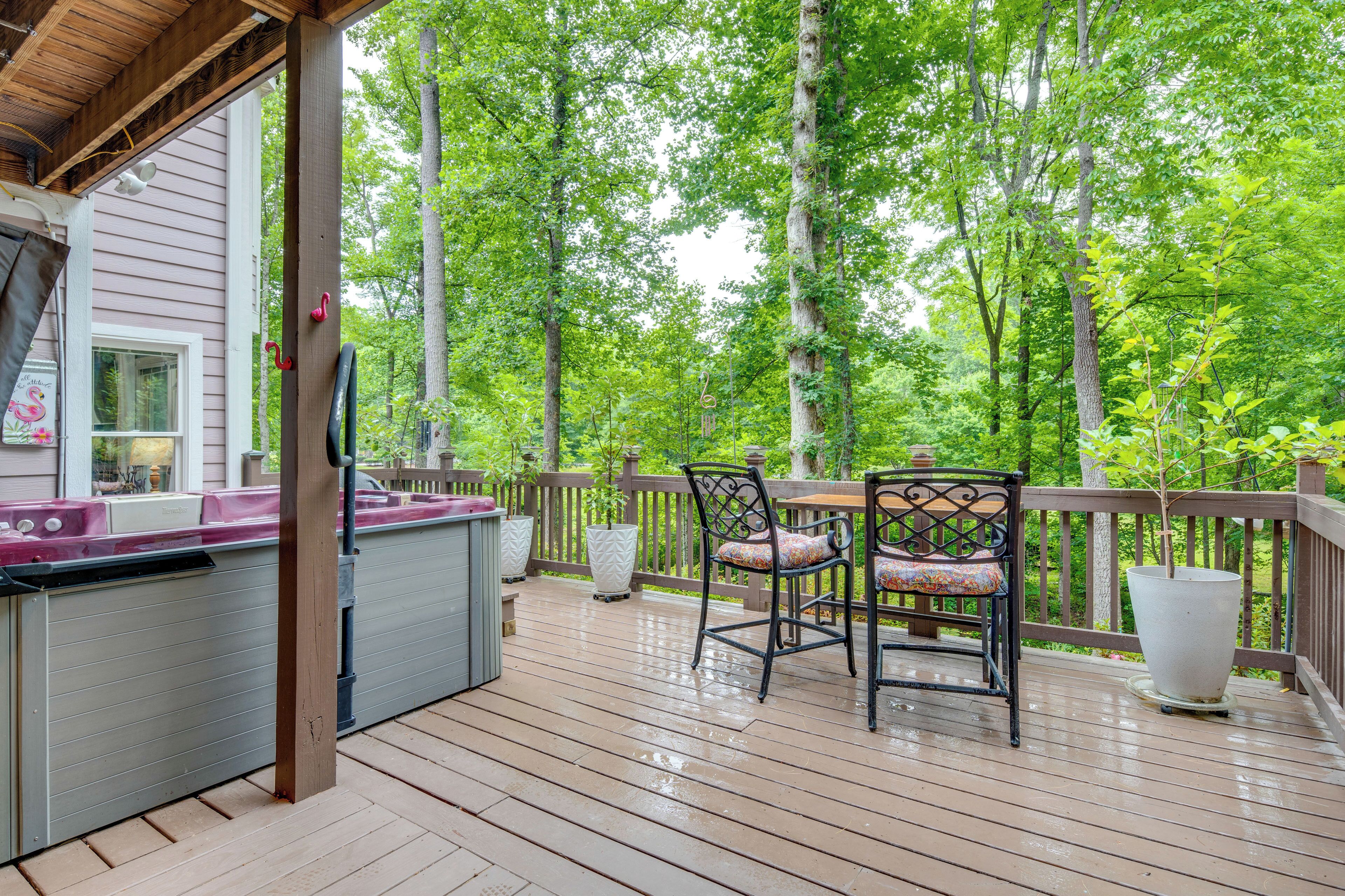 Une terrasse en bois avec un jacuzzi, deux chaises et un grand bac à fleurs.