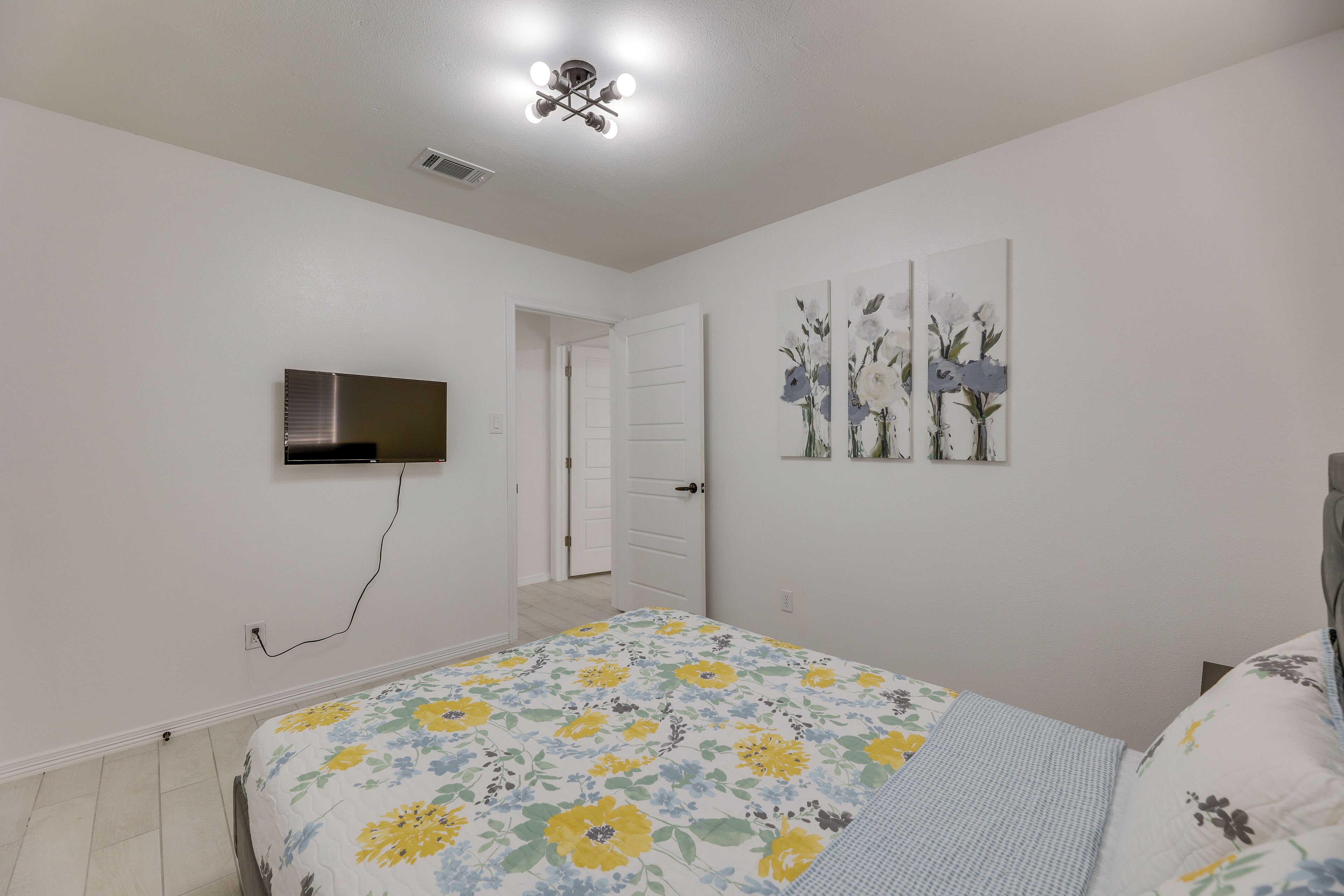 Un dormitorio con una cama, un televisor montado en la pared y una puerta que da a otra habitación.