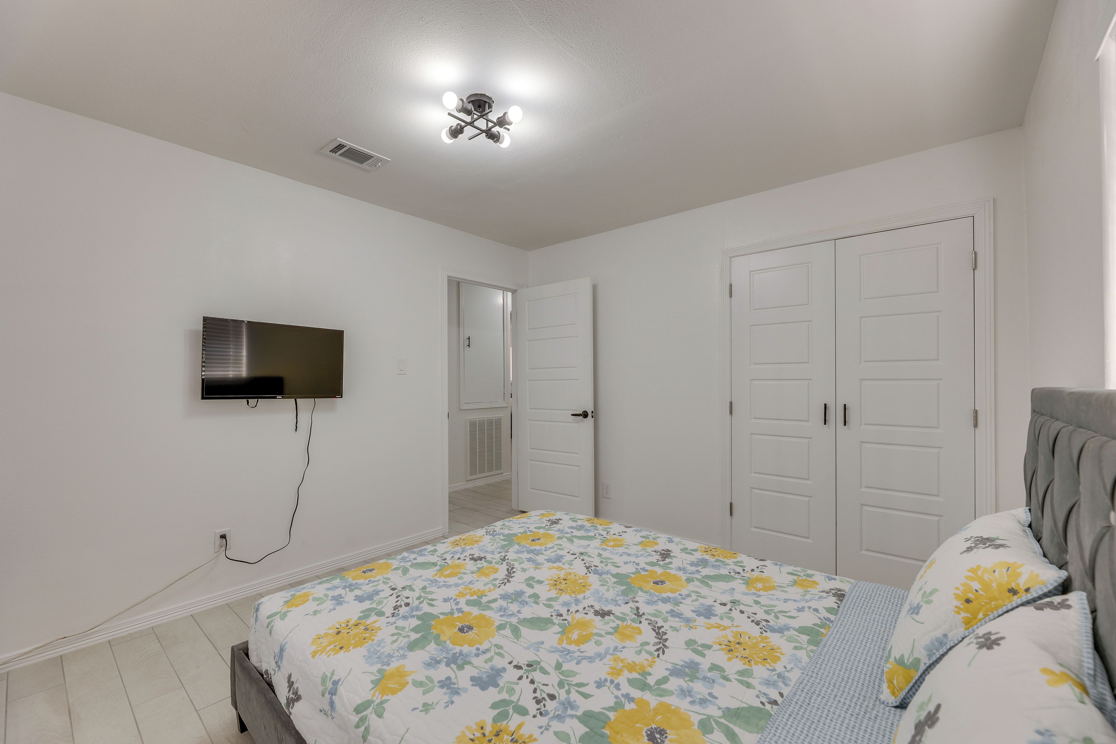 A bedroom with a bed, a television mounted on the wall, and a door leading to another room.