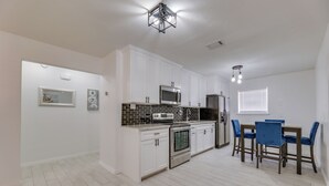 A modern kitchen with white cabinets, a built-in oven, a microwave, and a dining area with blue chairs. - Modern Home in Edinburg: Half-mi Walk to Utrgv! (Edinburg)
