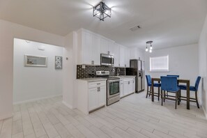 A modern kitchen with white cabinets, a built-in oven, a microwave, and a dining area with blue chairs. - Modern Home in Edinburg: Half-mi Walk to Utrgv! (Edinburg)
