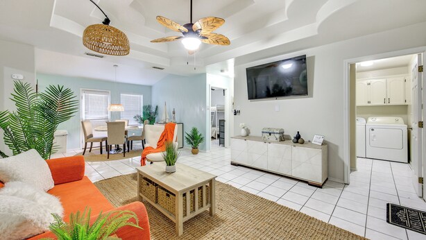 A modern living room with a sofa, coffee table, and ceiling fan. There is a dining area with chairs and a table, and a laundry room with appliances. - Welcoming Edinburg Apartment - Pet Friendly! (Edinburg)
