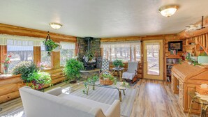 Ein gemütliches Blockhaus-Interieur mit einer Couch, Kamin, Holzwänden und großen Fenstern.