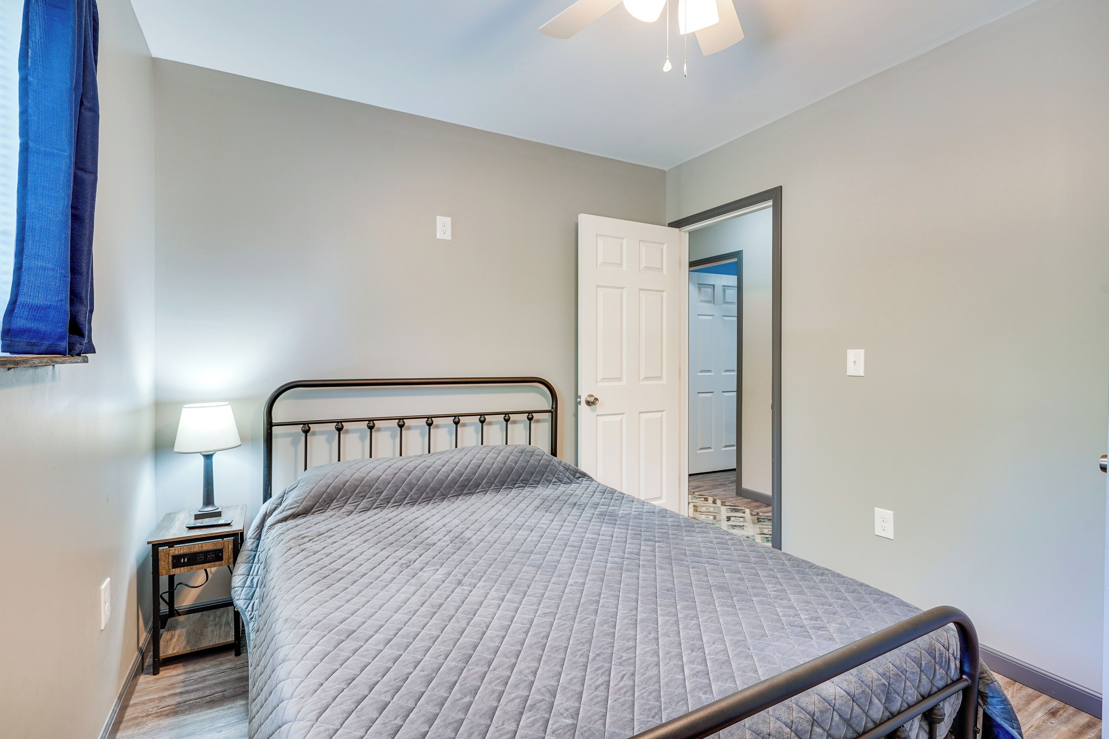 A bedroom with a bed, a nightstand, a lamp, and a door leading to another room.
