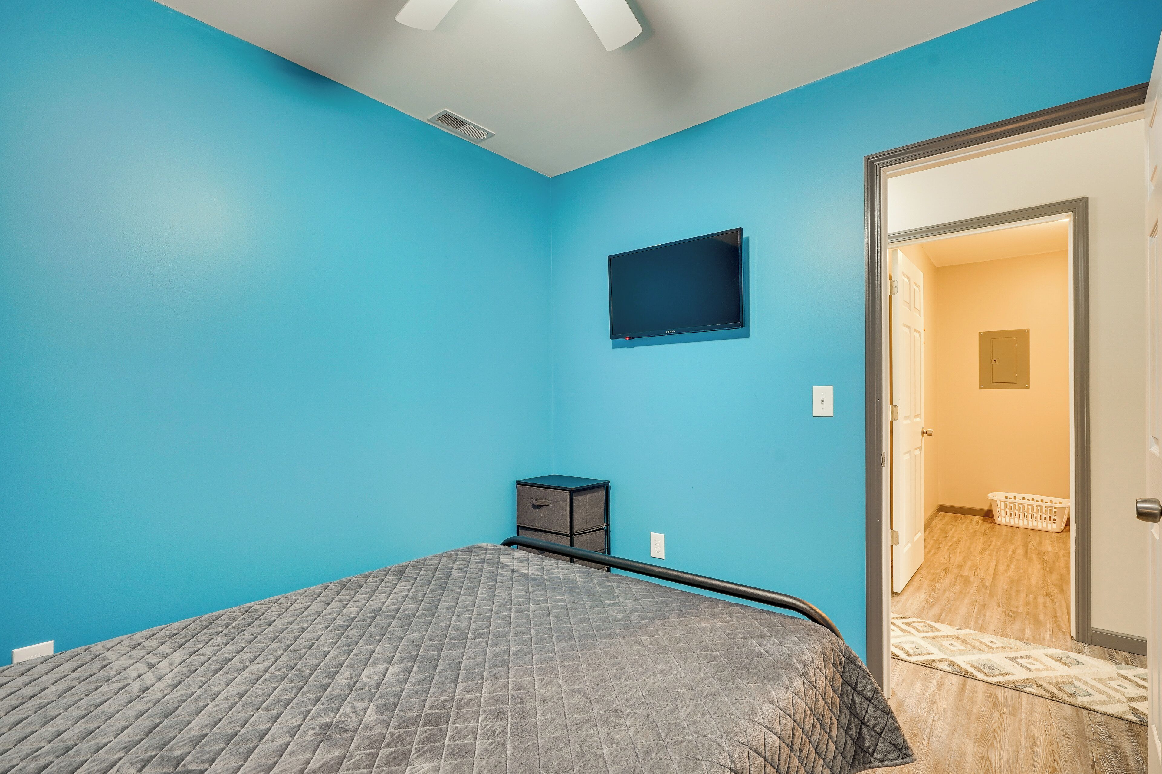 A bedroom with a bed, a television mounted on the wall, and a door leading to a laundry area.