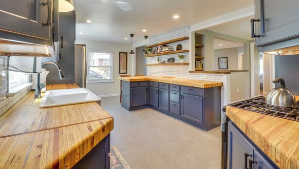 Una cucina moderna con mobili scuri, un piano di lavoro in legno e un piano cottura integrato.