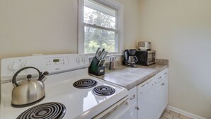 Una cucina con un piano cottura bianco, un bollitore, una macchina da caffè e una finestra sopra il bancone.