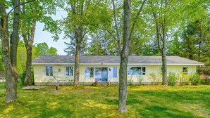 Une maison de plain-pied avec un porche à l’avant, entourée d’arbres et bordée d’une pelouse bien entretenue.