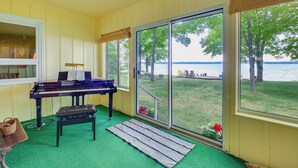 Un piano dans une pièce dotée d’une moquette verte, d’un banc et d’une vue sur un lac, visible à travers de grandes fenêtres.