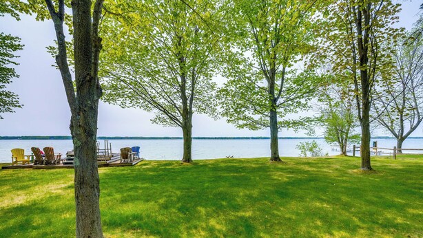 Une zone herbeuse avec des arbres et une jetée dotée de chaises, le tout au bord d’une étendue d’eau.