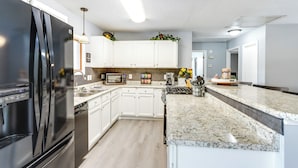 A modern kitchen with white cabinets, a black refrigerator, a granite countertop, and a microwave. - Fire Pit & Dock: Lake of the Ozarks Retreat! (Roach)