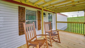 Un porche de madera con dos mecedoras, una ventana con contraventanas y vista a un campo verde.
