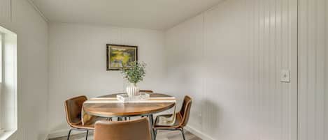 Een eethoek met een ronde tafel, twee stoelen, een vaas met een plant en een lijst met een afbeelding aan de muur.