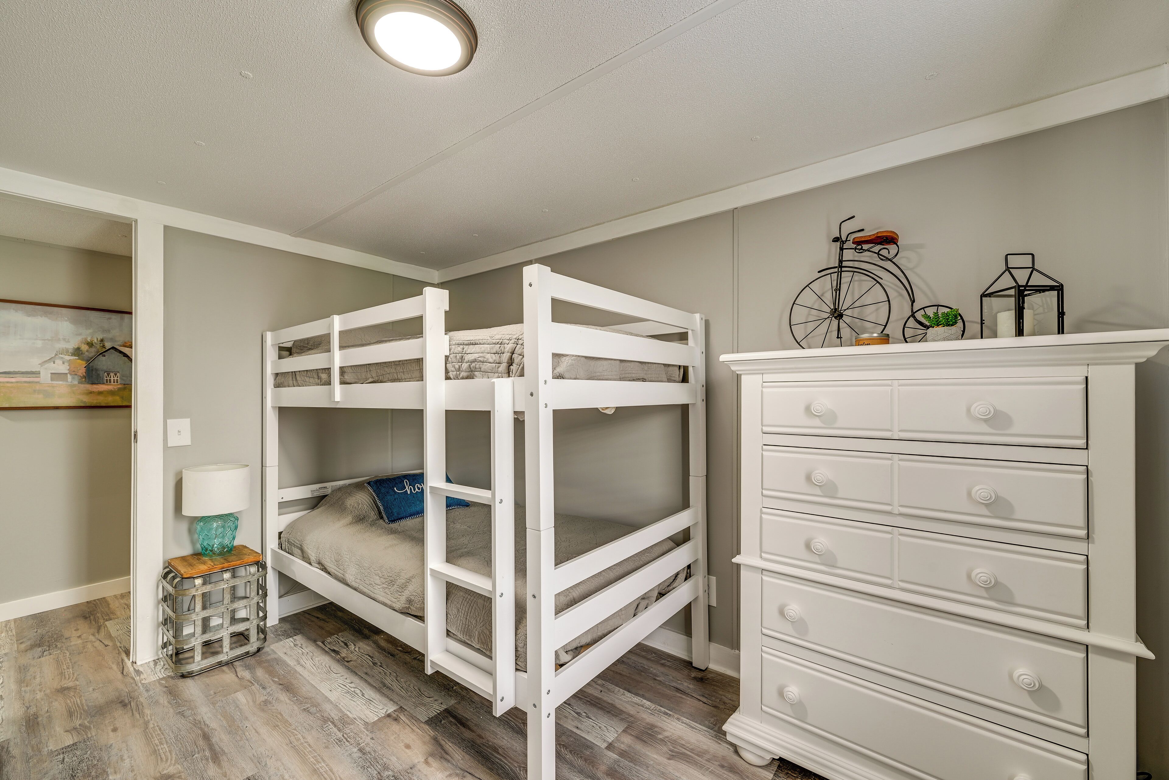 A bunk bed with a dresser and a lamp in a room with wooden flooring.