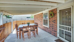 Een overdekt terras met een houten tafel en stoelen, een bakstenen muur en een deur met ruit.