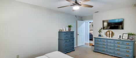 Un dormitorio con cama, cómoda, ventilador de techo y puerta que da a otra habitación.