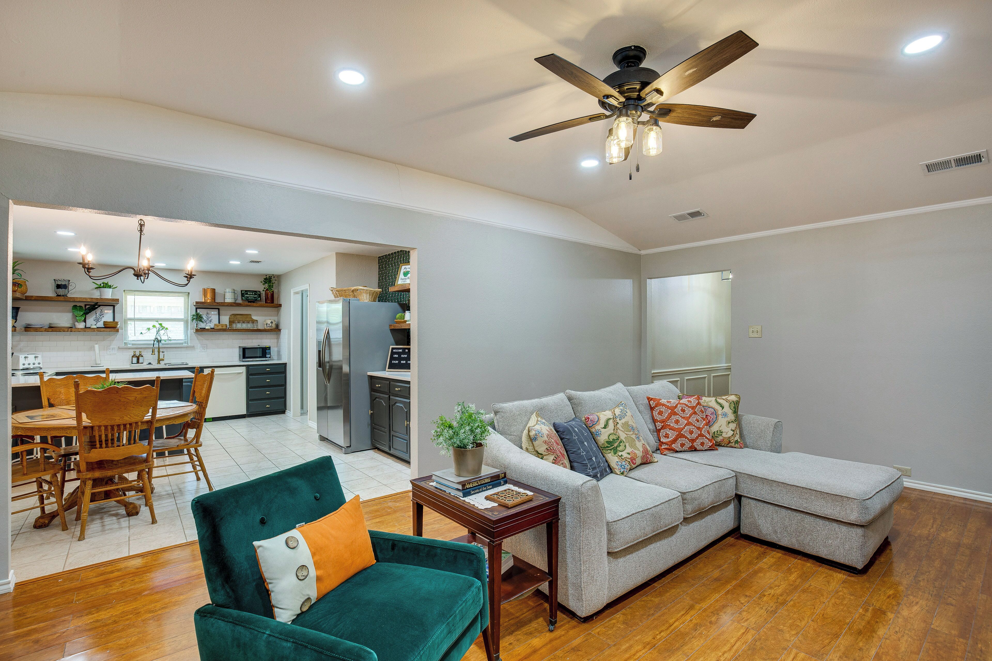 A spacious living room with a sectional sofa, a dining area with wooden chairs, and a kitchen in the background.