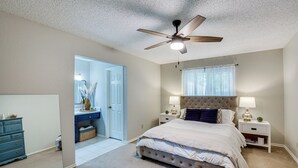 Een slaapkamer met een bed, nachtkastjes, een plafondventilator en een deur naar een andere kamer.