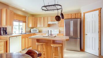 Una cocina moderna con armarios de madera, un refrigerador de acero inoxidable, un microondas y un colgador para ollas.