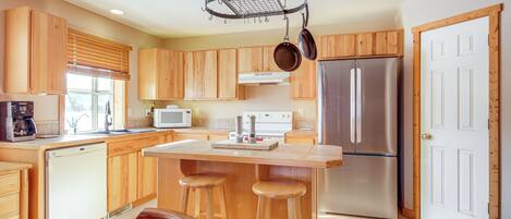 Una cocina moderna con armarios de madera, un refrigerador de acero inoxidable, un microondas y un colgador para ollas.