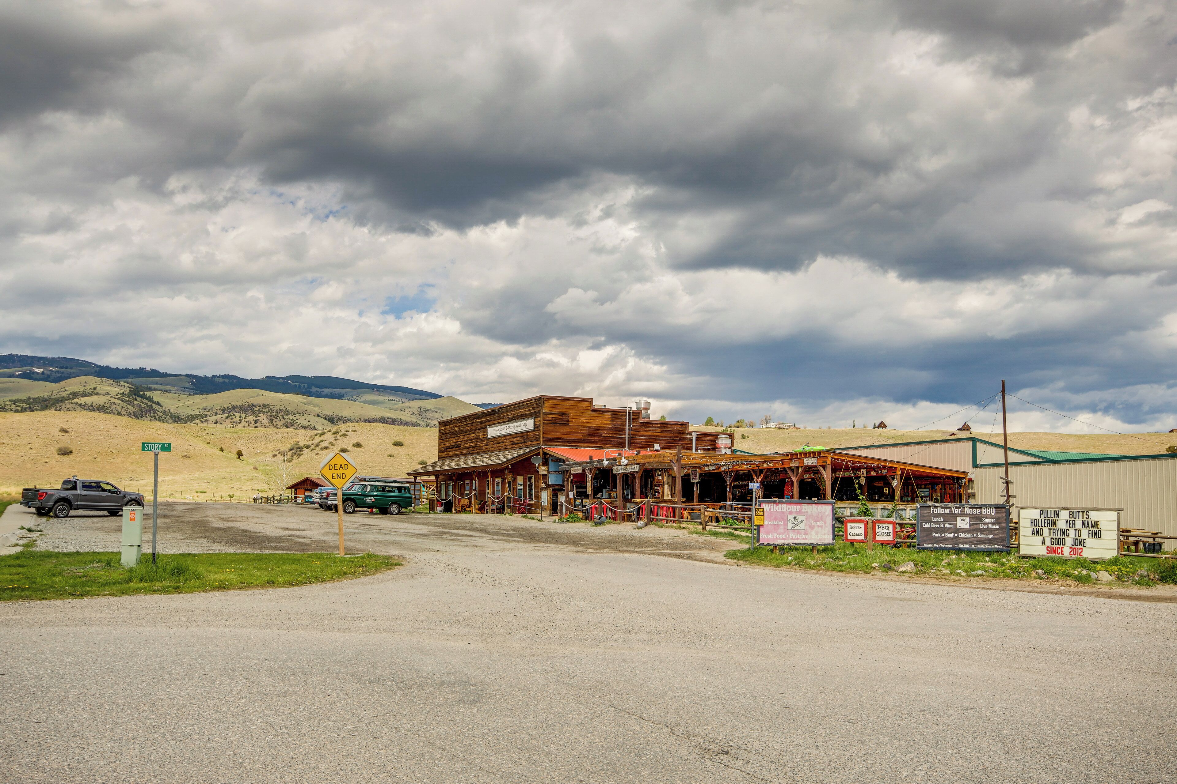 A rustic building with a wooden facade, a covered porch, and a signboard advertising a BBQ event.