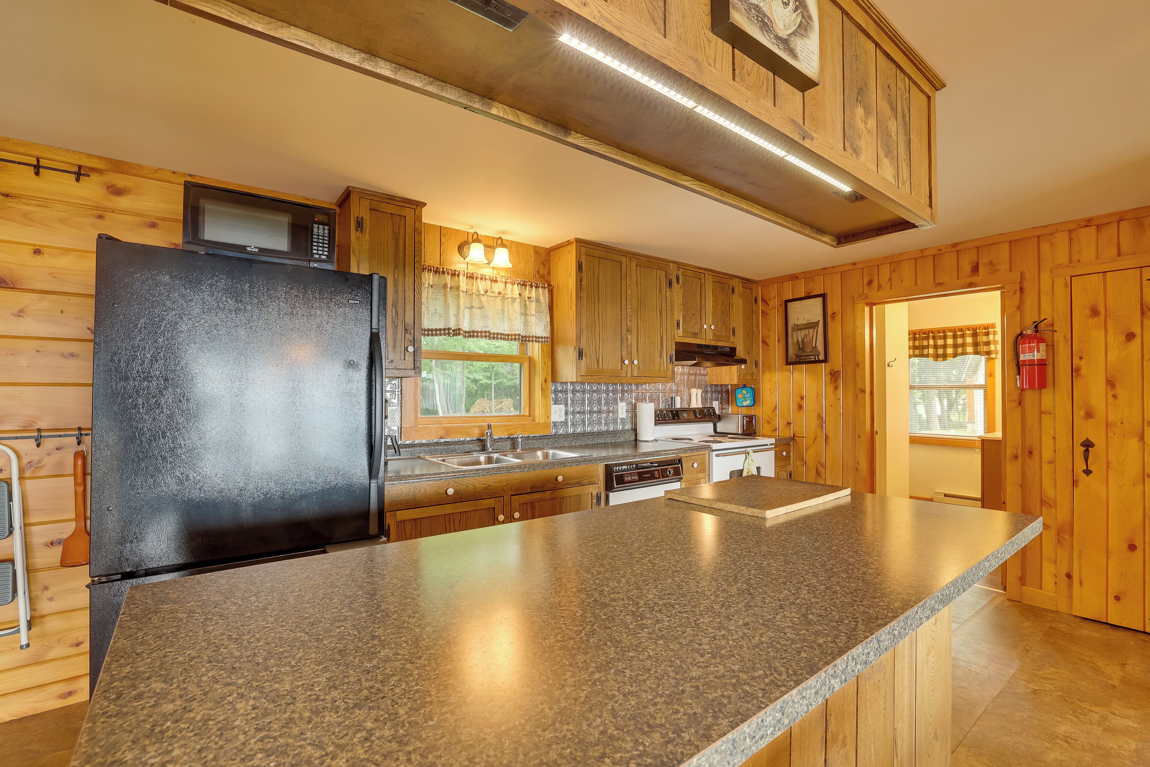 A kitchen with wooden cabinets, a granite countertop, a black refrigerator, a microwave, and a gas stove.