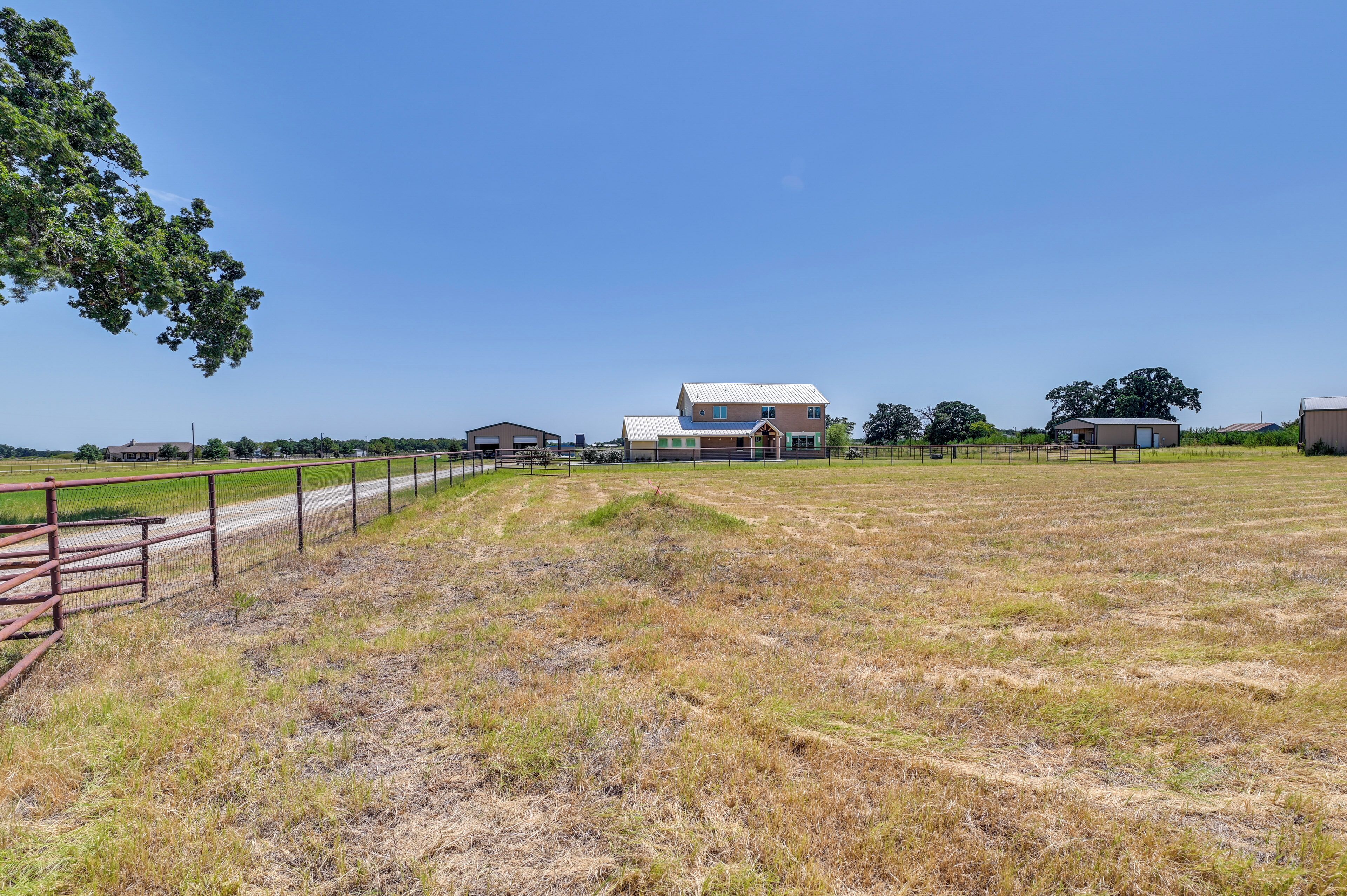 A large, open field with a metal fence and a building with a metal roof in the background.