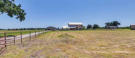 A large, open field with a metal fence and a building with a metal roof in the background.