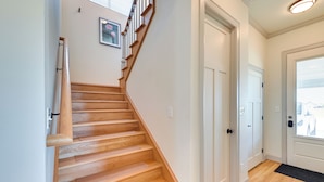 Un escalier en bois menant à une porte blanche, un tableau encadré accroché au mur et une fenêtre avec des stores.
