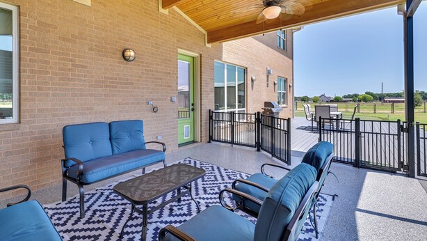 Un patio couvert avec un mur en briques, une porte verte et une vue sur une cour arrière aménagée avec du mobilier d’extérieur.