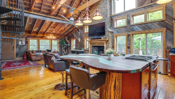 A spacious living area with a large wooden ceiling, a stone fireplace, and a bar area with stools. - Serene Pacific Getaway: Deck, Grill & Fire Pit! (Pacific)