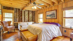 A wooden cabin bedroom with a bed, two chairs, a bench, a ceiling fan, and a painting on the wall. - Serene Pacific Getaway: Deck, Grill & Fire Pit! (Pacific)